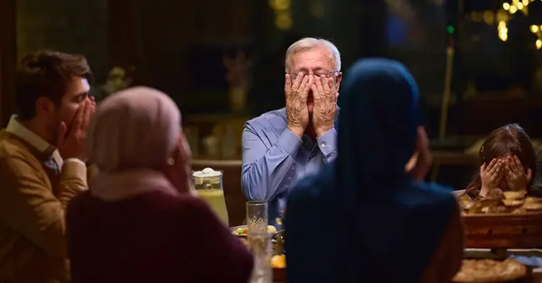 stock image In a modern restaurant setting, a European Islamic family comes together for iftar during Ramadan, engaging in prayer before the meal, uniting tradition and contemporary practices in a celebration of