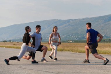 Kararlı bir grup sporcu koşularından önce kolektif bir esneme oturumuna katılıyor, takım çalışmasını teşvik ediyor ve fitness hedeflerini gerçekleştirmek için hazırlık yapıyorlar..