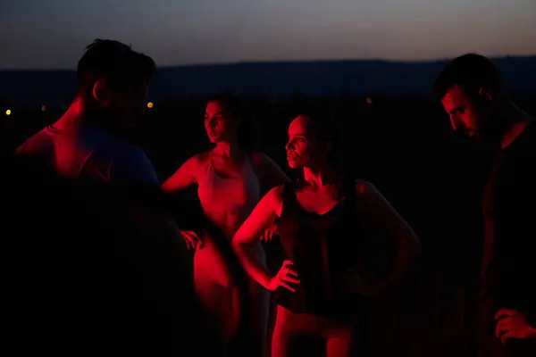 stock image In the late-night hours, a diverse group of exhausted athletes find solace under a red glow, reflecting on their day-long marathon journey and celebrating camaraderie amidst fatigue.