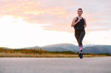 Kararlı bir sporcu güneşin altında kendinden emin bir şekilde koşar. Çevresi göz kamaştırıcı doğal manzaralarla çevrilidir. Zindelik arayışında güç ve direnç gösterir. 