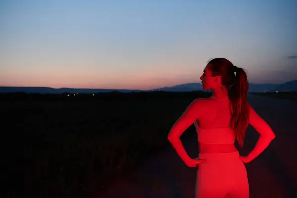 stock image After a grueling nighttime run, an athlete strikes a confident pose, bathed in the red glow of the surroundings, showcasing both exhaustion and determination.