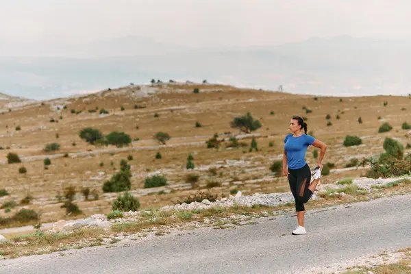 Stock image A determined female athlete stretches her muscles after a strenuous run through rugged mountain terrain, surrounded by breathtaking rocky landscapes. 