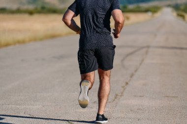 Atletik bir adam güneşin altında koşar, vücudunu yaşam şartlarına şartlandırır. Önündeki yolculuk için azim ve güç yayar.