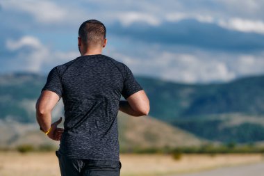 Atletik bir adam güneşin altında koşar, vücudunu yaşam şartlarına şartlandırır. Önündeki yolculuk için azim ve güç yayar.