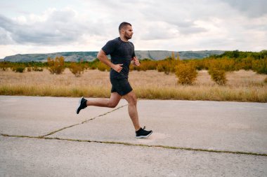 Atletik bir adam güneşin altında koşar, vücudunu yaşam şartlarına şartlandırır. Önündeki yolculuk için azim ve güç yayar.