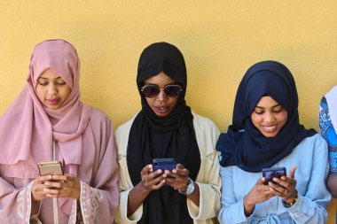 Çeşitli gençlerden oluşan bir grup, akıllı telefonlarına dalmış, modern bağlantılarını ve sosyal etkileşimlerini sergiliyorlar..