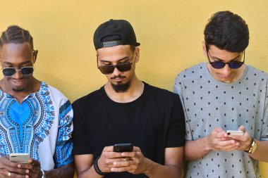 A diverse group of teenagers standing together against a wall, engrossed in their smartphones, showcasing modern connectivity and social interaction. clipart