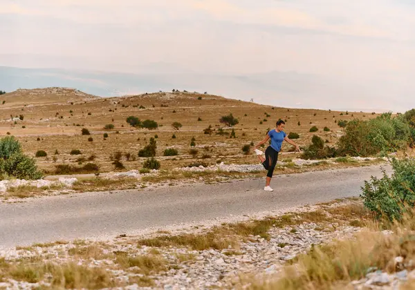 Kararlı bir dişi atlet, engebeli dağ arazilerinde nefes kesici kaya manzaralarıyla çevrili yorucu bir koşudan sonra kaslarını esnetir.. 