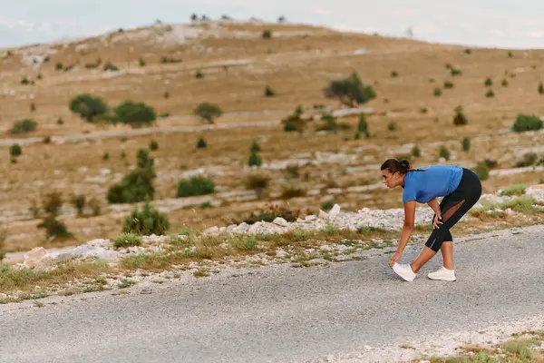 stock image A determined female athlete stretches her muscles after a strenuous run through rugged mountain terrain, surrounded by breathtaking rocky landscapes. 