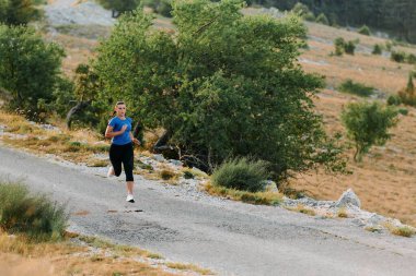 Kararlı bir bayan atlet gün doğumunda ormanda koşuyor, nefes kesici doğal güzellik ve canlı yeşillik ile çevrili.. 
