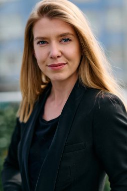 Çarpıcı bir portre siyah takım elbiseli, özgüvenli ve zarif bir iş kadını yakalıyor, terasta zarif bir şekilde poz veriyor hareketli şehir manzarasının arka planına karşı.