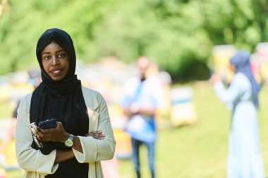  Orta Doğulu tesettürlü Müslüman kadın, küçük bir arıcılık işini yönetirken akıllı telefon kullanıyor, modern teknolojiyi geleneksel uygulamalarla harmanlıyor.