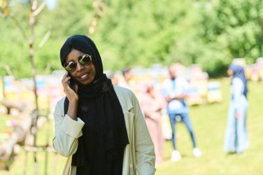  Orta Doğulu tesettürlü Müslüman kadın, küçük bir arıcılık işini yönetirken akıllı telefon kullanıyor, modern teknolojiyi geleneksel uygulamalarla harmanlıyor.