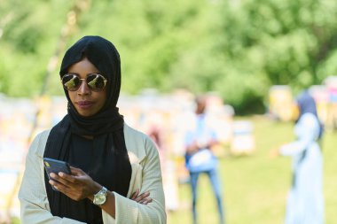  Orta Doğulu tesettürlü Müslüman kadın, küçük bir arıcılık işini yönetirken akıllı telefon kullanıyor, modern teknolojiyi geleneksel uygulamalarla harmanlıyor.