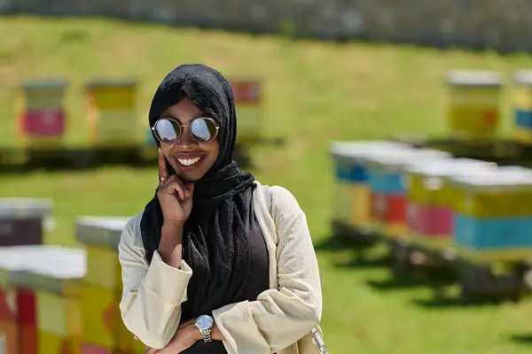 stock image African American Muslim woman in hijab explores natural bee farms for honey production, blending tradition with sustainability in the serene countryside. 