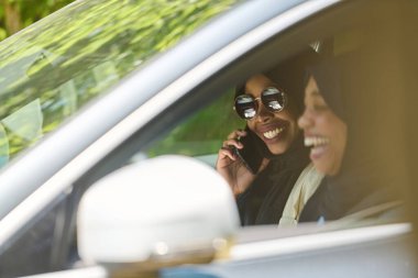 Başörtüsü takan iki Müslüman kadın, bir arabada seyahat ederken akıllı bir telefonla sohbet ediyorlar..