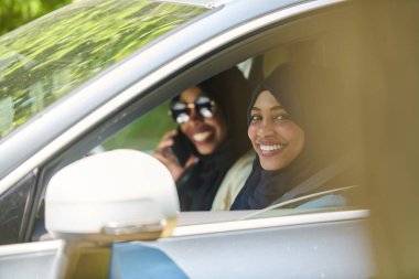 Başörtüsü takan iki Müslüman kadın, bir arabada seyahat ederken akıllı bir telefonla sohbet ediyorlar..