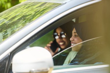 Başörtüsü takan iki Müslüman kadın, bir arabada seyahat ederken akıllı bir telefonla sohbet ediyorlar..