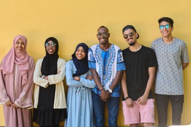 Afro-Amerikan ve Ortadoğu gençlerinden oluşan çeşitli bir grup canlı sarı bir duvarın önünde güvenle duruyor, birlik ve kentsel tarzı sergiliyorlar.
