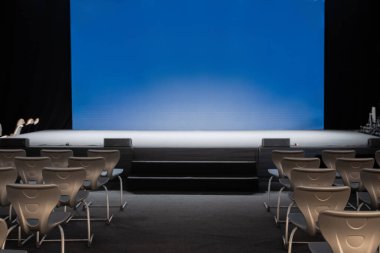 Boş bir konferans sahnesi, sıra sıra sandalyeler ve boş bir mavi ekran, bir seminer veya konferans ortamının beklentisini ve potansiyelini yakalamaya hazır. işletme eğitimi kavramı