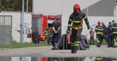 İtfaiyecilerden oluşan bir ekip, yangın söndürme görevine hazırlanmak için acilen su hortumlarını hazırlıyor ve yangın söndürme ve güvenliğe olan bağlılıklarını vurguluyor.