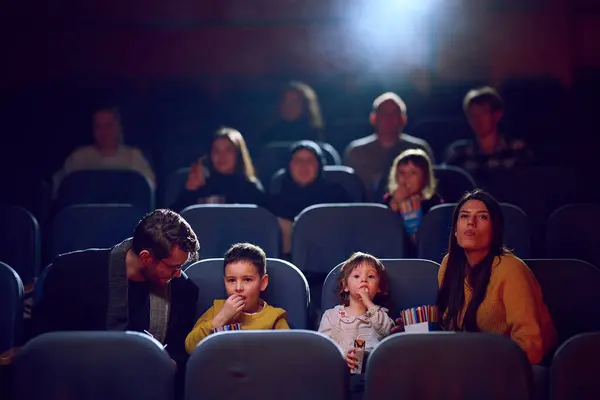 Stock image A modern family enjoys quality time together at the cinema, indulging in popcorn while watching a movie with their children.