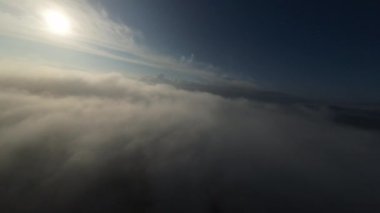 Dağlarda taze bir sabahta inanılmaz güzel bir bulutun içinden uçmak. Beyaz tüylü bulutlardan oluşan FPV insansız hava aracı açık mavi gökyüzünde usulca hareket ediyor