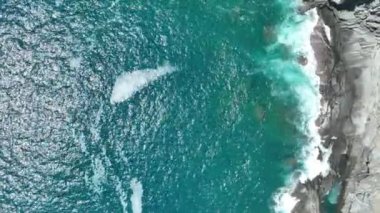 Engebeli, kayalık kıyı şeridini yıkayan turkuaz okyanus sularının hava görüntüleri. Deniz dalgaları kıyıya vuruyor. Yukarıdan görünüyor. Yüksek kalite sinematik yavaş çekim görüntüleri.