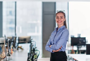 Profesyonel bir ortamda, sarışın bir iş kadını kendinden emin bir liderlik sergiliyor, otoritesini ve kararlılığını kollarını kavuşturarak iletiyor.. 