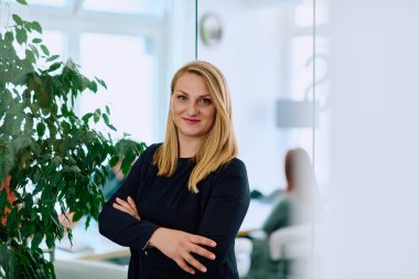 Dengeli esmer bir iş kadını, kollarını şık ve modern ofis binasının önünde kavuşturarak güvenle ayakta duruyor.. 