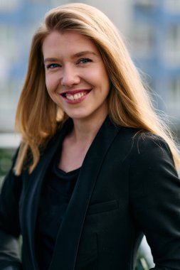 Çarpıcı bir portre siyah takım elbiseli, özgüvenli ve zarif bir iş kadını yakalıyor, terasta zarif bir şekilde poz veriyor hareketli şehir manzarasının arka planına karşı.