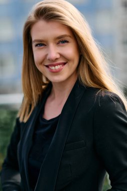 Çarpıcı bir portre siyah takım elbiseli, özgüvenli ve zarif bir iş kadını yakalıyor, terasta zarif bir şekilde poz veriyor hareketli şehir manzarasının arka planına karşı.