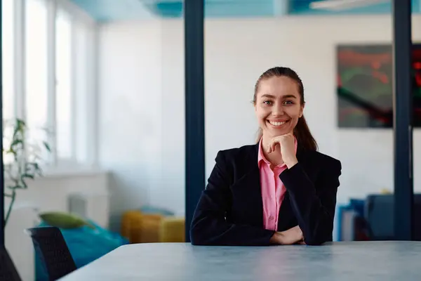 stock image Successful young female leader in a suit with a pink shirt sitting in a modern glass office with a determined smile