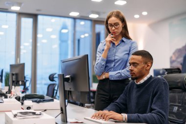 Çağdaş bir ofis ortamında, sarışın bir iş kadını ve onun Afrikalı Amerikalı iş ortağı, internetteki belgelere odaklanmış bir kararlılıkla bakıyorlar.