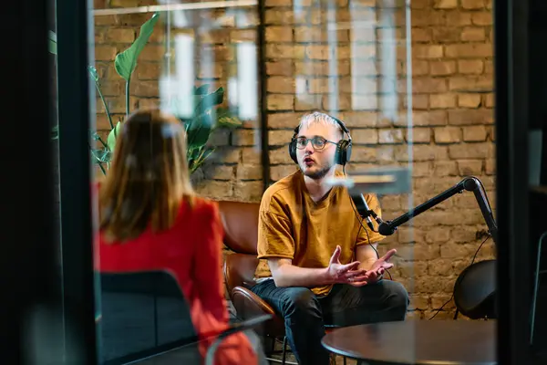 stock image A gathering of young business professionals, some seated in a glass-walled office, engage in a lively conversation and record an online podcast, embodying modern collaboration and dynamic interaction