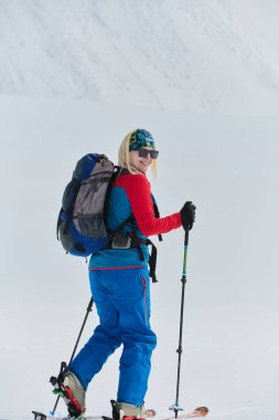 Kararlı bir kayakçı Alplerde karlı bir zirveye tırmanır, destansı bir iniş için taşıma gereçleri taşır.