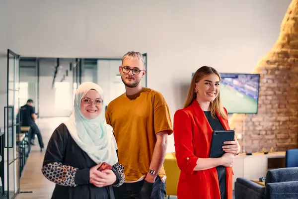 Stock image A group of young business colleagues, including a woman in a hijab, stands united in the modern corridor of a spacious startup coworking center