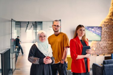 Aralarında tesettürlü bir kadının da bulunduğu bir grup genç iş arkadaşı, geniş bir iş ortaklığı merkezinin modern koridorunda birleşik duruyor.