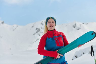 Başarılı bir bayan kayakçı, zorlu bir tırmanışı fethettikten sonra karlı bir zirvenin tepesinde kendine güvenle ışıldar.. 