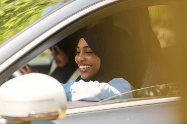 Two Muslim women wearing hijab converse on a smartphone while traveling together in a car through the. clipart