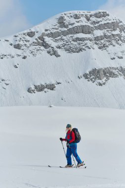 A determined skier scales a snow-capped peak in the Alps, carrying backcountry gear for an epic descent clipart