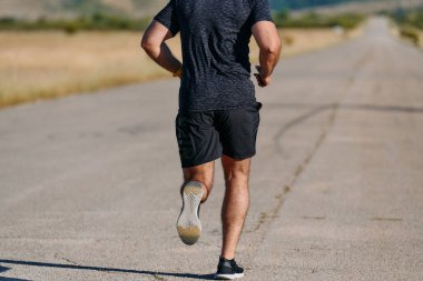 Atletik bir adam güneşin altında koşar, vücudunu yaşam şartlarına şartlandırır. Önündeki yolculuk için azim ve güç yayar.