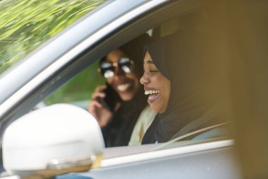 Başörtüsü takan iki Müslüman kadın, bir arabada seyahat ederken akıllı bir telefonla sohbet ediyorlar..