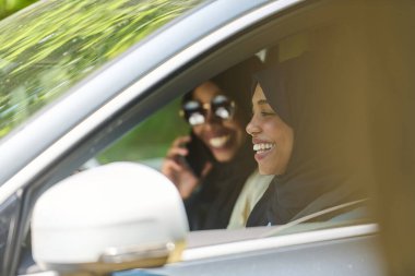 Başörtüsü takan iki Müslüman kadın, bir arabada seyahat ederken akıllı bir telefonla sohbet ediyorlar..
