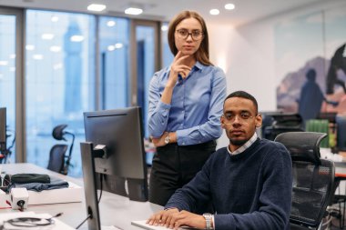 Çağdaş bir ofis ortamında, sarışın bir iş kadını ve onun Afrikalı Amerikalı iş ortağı, internetteki belgelere odaklanmış bir kararlılıkla bakıyorlar.