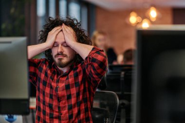Dağınık saçlı bir programcı oturur, bilgisayar monitörüne hayal kırıklığı dolu bir bakışla bakar, teknik zorlukları yansıtır..