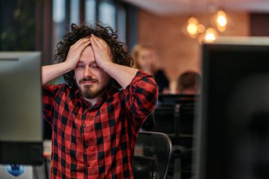 Dağınık saçlı bir programcı oturur, bilgisayar monitörüne hayal kırıklığı dolu bir bakışla bakar, teknik zorlukları yansıtır..
