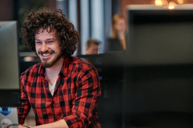 Afro saç stili ve ekose gömlekli bir programcı, modern ofis ortamındaki bir bilgisayarda özenle kodluyor.