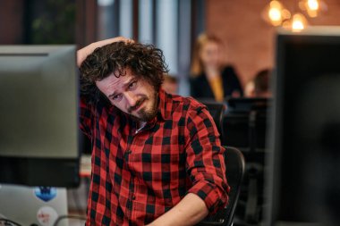 Dağınık saçlı bir programcı oturur, bilgisayar monitörüne hayal kırıklığı dolu bir bakışla bakar, teknik zorlukları yansıtır..