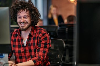 Afro saç stili ve ekose gömlekli bir programcı, modern ofis ortamındaki bir bilgisayarda özenle kodluyor.